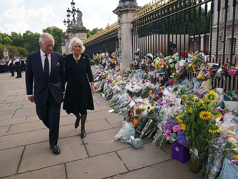 König Charles III. und seine Frau Camilla sehen sich die Blumengestecke an, die nach dem Tod von Königin Elizabeth II. vor dem Buckingham-Palast abgelegt wurden. Foto: Yui Mok/PA Wire/dpa
